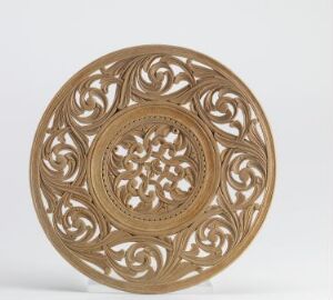  Intricately carved circular wooden plate with symmetrical floral motifs and openwork patterns on a light-gray background. Artist's name and title of the piece are unknown.