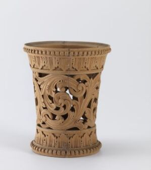  An intricately carved light brown cylindrical container with delicate openwork patterns of swirls and florals on a soft white background. Artist name and title are unknown.