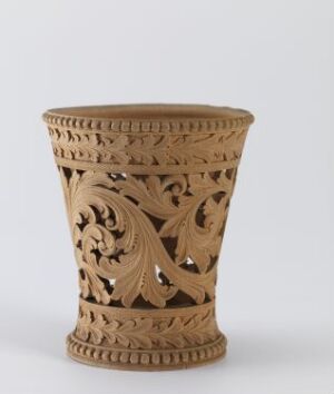  A warm, tawny-colored ceramic vase with intricate openwork carving displaying stylized foliage and geometric patterns stands against a light grey background. The vase has a flared shape with a decorative band around the top edge, showcasing traditional craftsmanship.