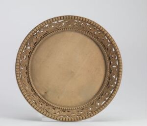  A circular, metal plate with an intricately detailed and perforated rim, displaying a bronzy gold color set against a neutral background. The center is smoother and lighter in color, while the decorative rim has embossed leaf-like patterns and cutout details.