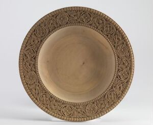  A round, shallow, sandy brown or tan ceramic bowl with an intricately etched pattern on the wide brim, positioned against a neutral background.