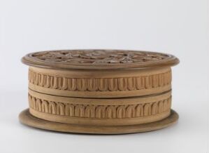  A cylindrical, wooden-looking object with intricate decorative bands, including a classical column-like pattern on the lower part and a floral motif on the upper part, set against a plain light background.