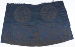  A piece of aged navy blue textile with two large, circular patterns with intricate lighter blue and rust-colored motifs against a neutral, blurred background.