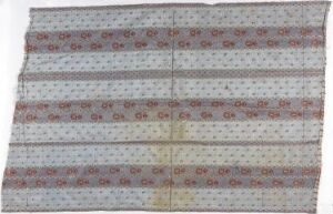  A rectangular, aged-looking fabric with a light gray background, featuring repeating horizontal bands of red, orange, brown, and teal circular motifs with geometric and floral designs, showing creases and discoloration indicative of age or use.