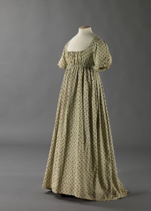  An antique dress with an Empire waistline and a small, dark motif print on a light base color, presented on a mannequin against a gray background.