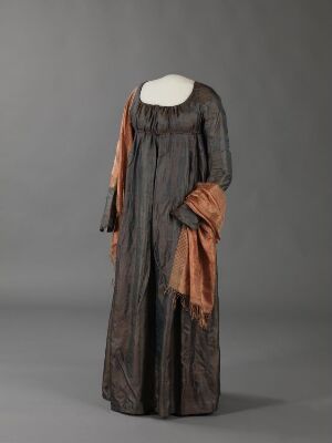  A mannequin displays a vintage full-length dress with vertical chocolate brown and caramel stripes, sheer long puffed sleeves, and a burnt orange waist sash, set against a gray background.