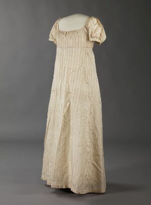  An antique off-white Empire waist dress with delicate puff sleeves and detailed vertical pleating on the bodice and skirt, displayed against a dark grey background.