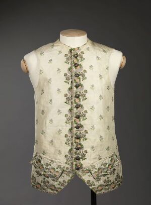  A sleeveless, high-collared vintage vest with intricate green floral and foliage patterns on an off-white background, displayed on a mannequin torso against a neutral grey backdrop.