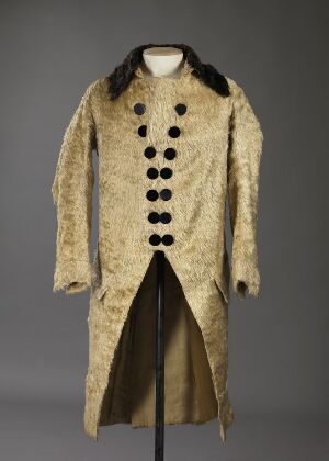  A historical beige wool coat with a black collar and double row of black buttons on a mannequin, set against a gray background. The coat has a tailcoat split and a formal, military-style cut from either the 18th or 19th century.