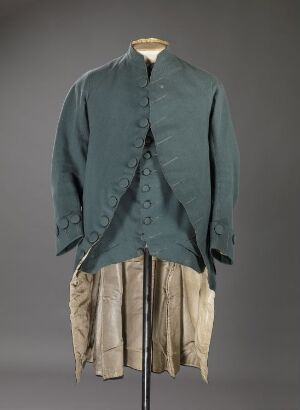  Antique faded teal coat with fabric-covered buttons over off-white knee-length breeches on a fabric-covered mannequin against a dark gray background, representing an 18th-century man's suit.