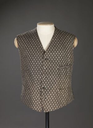  A tailored sleeveless vest with a geometric pattern in muted shades of brown or grey, with polished buttons, displayed on a mannequin against a dark background.