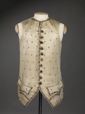  Antique creamy off-white gentleman's waistcoat with dark brown or black embellishments and buttons on a torso mannequin against a dark grey background.