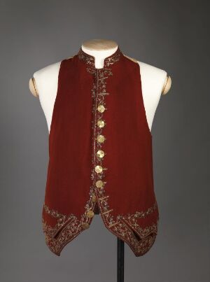  A regal-looking, sleeveless, burgundy waistcoat with golden buttons and intricate gold, white, and brown floral embroidery along the edges, displayed on a mannequin stand against a gray background.