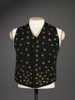 
 A sleeveless, V-neck formal vest with a black base color, decorated with a uniform pattern of small gold floral or star-like motifs, displayed on a mannequin against a gray background.