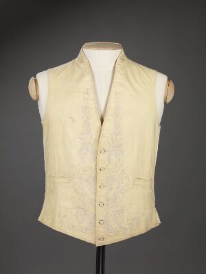  A cream-colored, sleeveless waistcoat with a floral pattern and small buttons displayed on a mannequin torso against a gray background.