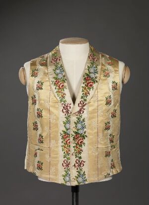  A cream-beige embroidered vest with floral patterns in red, green, yellow, and blue, displayed on a mannequin against a neutral gray background. Artist name and title unknown.