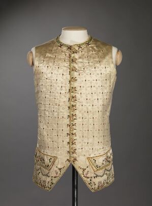  An ivory or cream-colored sleeveless vest with detailed floral embroidery displayed on a mannequin torso against a gray background, featuring ornamental buttons along the front.