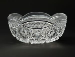  An elegant crystal bowl with a scalloped edge and intricate cut-glass patterns, set against a dark background.