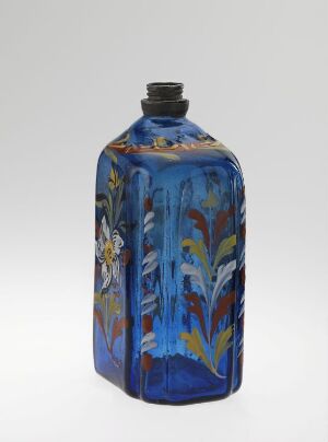  An ornate cobalt blue glass bottle with a black cap and colorful floral patterns in yellow, white, green, and red hues against a neutral background. Artist name and title are unknown.