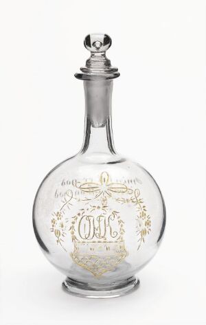  An intricate gold-decorated clear glass decanter with a spherical body, slender neck, and matching stopper, embossed with the letters "O.H.C." on a neutral white background.