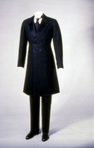  A mannequin wearing a formal navy blue double-breasted coat over matching trousers with a pair of glossy black shoes, showcased against a light gray background.