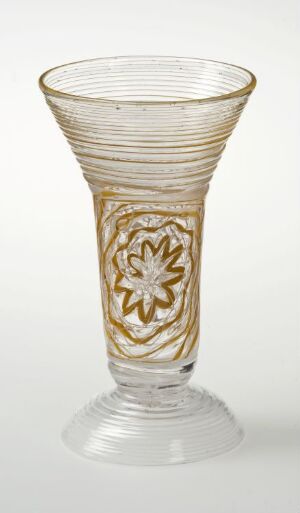  A delicate, translucent glass with a flared rim, adorned with horizontal texture bands and a central golden floral motif, on a plain background.