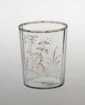  A clear glass cup with delicate botanical engravings set against a light gray background, highlighting its simple elegance and fine details.