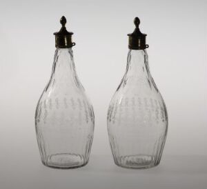  Two identical vintage clear glass bottles with ribbed textures and dark metallic screw-on stoppers, set against a gradient gray background.