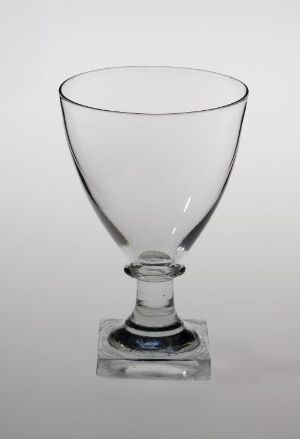  A clear glass goblet with a wide bowl and a short stem attached to a flat, disc-shaped foot, displayed against a light gray background.
