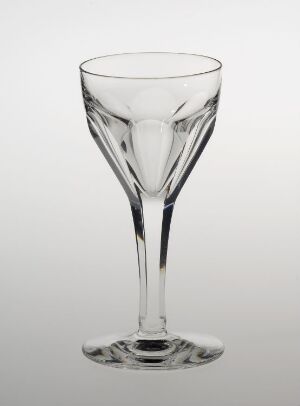  A single, elegant, clear wine glass with a slender stem stands against a gradient light grey background, showcasing its simple design and transparent material.