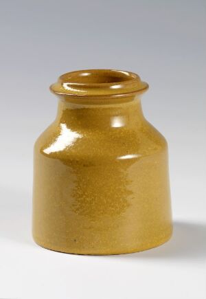  A ceramic jar with a glossy honey-colored glaze on a light background. The jar has a rounded base and flared rim, with visible glaze drips creating a pattern on its midsection.