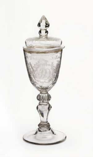  An elegant, clear glass goblet with a lid, featuring a decorative finial on top and etched designs on the bowl, set against a light background. Artist name and title are unknown.