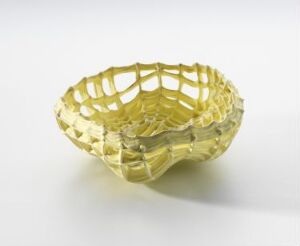  A delicate porcelain bowl titled "Rede gult" by artist Sidsel Hanum, featuring a vibrant yellow lattice design with a glossy finish, demonstrating intricate craftsmanship and artistic design in its porous nest-like structure.