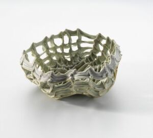  "Rede gønt," a porcelain bowl designed by Sidsel Hanum, with an intricate, openwork nest-like structure in an earthy green hue with beige undertones, showcasing a delicate balance between artistry and functionality.