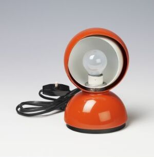 
 "Eclisse" by Vico Magistretti, a lacquered cast metal and plastic lamp featuring a vibrant orange dome-shaped base with an adjustable white inner shade, an exposed bulb, and a black electrical cord.