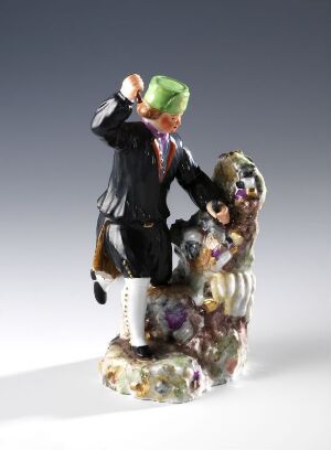  A detailed figurine featuring two characters: a man with green hair in a black tuxedo on the left, and a colorful, flowerlike entity on the right, all against a plain, light background.