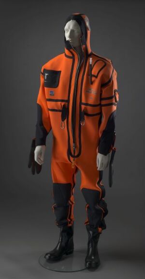  A life-saving costume designed by Helge M. Hansen, primarily bright orange with black detailing, featuring multiple layers of synthetic rubber, metal zippers, and plastic parts, displaying high visibility and durability, machine-made and glued, with machine-stitched, laminated seams for enhanced resistance, accompanied by black gloves and boots, all against a subdued gray background.