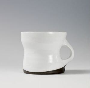  A white ceramic cup with a flared rim and attached handle, set against a light grey background, featuring a subtle unglazed brown ring at its base.