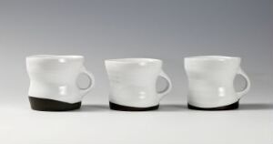  Three white ceramic coffee mugs with black-glazed bases, lined up on a flat surface against a soft gradient background transitioning from light gray to white.