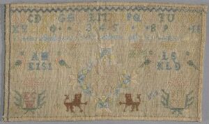  An antique fabric sampler with faded beige background featuring embroidered alphabets, symmetrical flower and bird motifs in pastel colors, and two stylized lion-like animals, reflecting historical needlework practices.