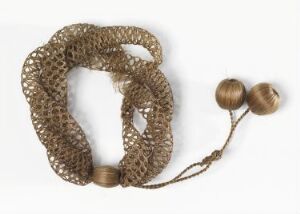  An ornate object with a textured golden-brown mesh loop and two smooth, spherical elements connected by a delicate strand, displayed against a light beige background.