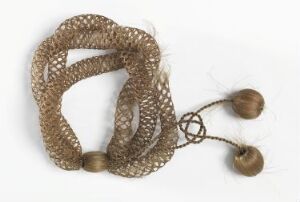  A handcrafted piece of jewelry or decoration consisting of earthy brown interlocking loops of net-like material with four dark brown polished spherical beads attached by thin twine strings against an off-white background.