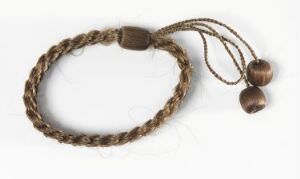  A handmade braided bracelet with a natural, rustic appearance, featuring a spectrum of brown tones from light tan to dark brown, with two polished beads on one end and a thin, darker string with two additional beads at the tips.