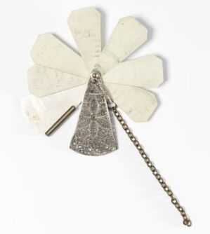  A vintage, cream-colored paper fan with a decorative metallic handle and a small chain, unfolded to display its radially arranged, leaf-shaped blades with faded writing.