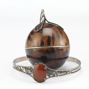  A beautiful jewelry piece featuring a polished, spherical tiger's eye orb pendant displayed on an intricate silver-colored bracelet stand with an amber-colored oval gem setting.