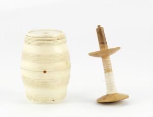  Two wooden objects on a white background; on the left, a small barrel-like object with horizontal ridges, and on the right, a traditional spinning top with a long, slender shaft and a round base, both crafted from light-colored woods.