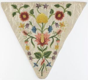  An embroidered, cream-colored triangular fabric with a vibrant floral pattern featuring red, yellow, and blue flowers with green leaves.