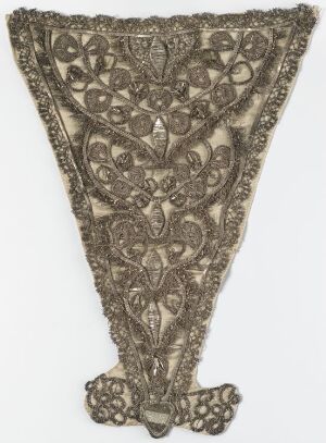  An intricate, V-shaped, decorative piece with a symmetrical lace-like pattern featuring floral and foliage motifs in muted silver or grayish-taupe hues, suggesting an antique textile or handcrafted artwork.