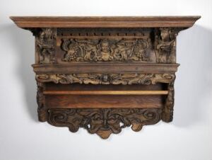  An antique wooden shelf with detailed carvings of figures and floral patterns, a rich brown in color set against a neutral light greyish-tan background.