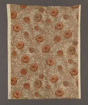  An ornate, beige-colored textile or paper featuring a dense, dark brown mesh-like pattern with regularly spaced rust or amber-colored floral motifs with scalloped edges, suggesting a vintage or traditional style.